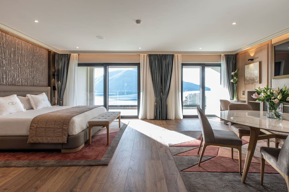 A modern hotel room with a large bed, a dining table, and a view of the sea.