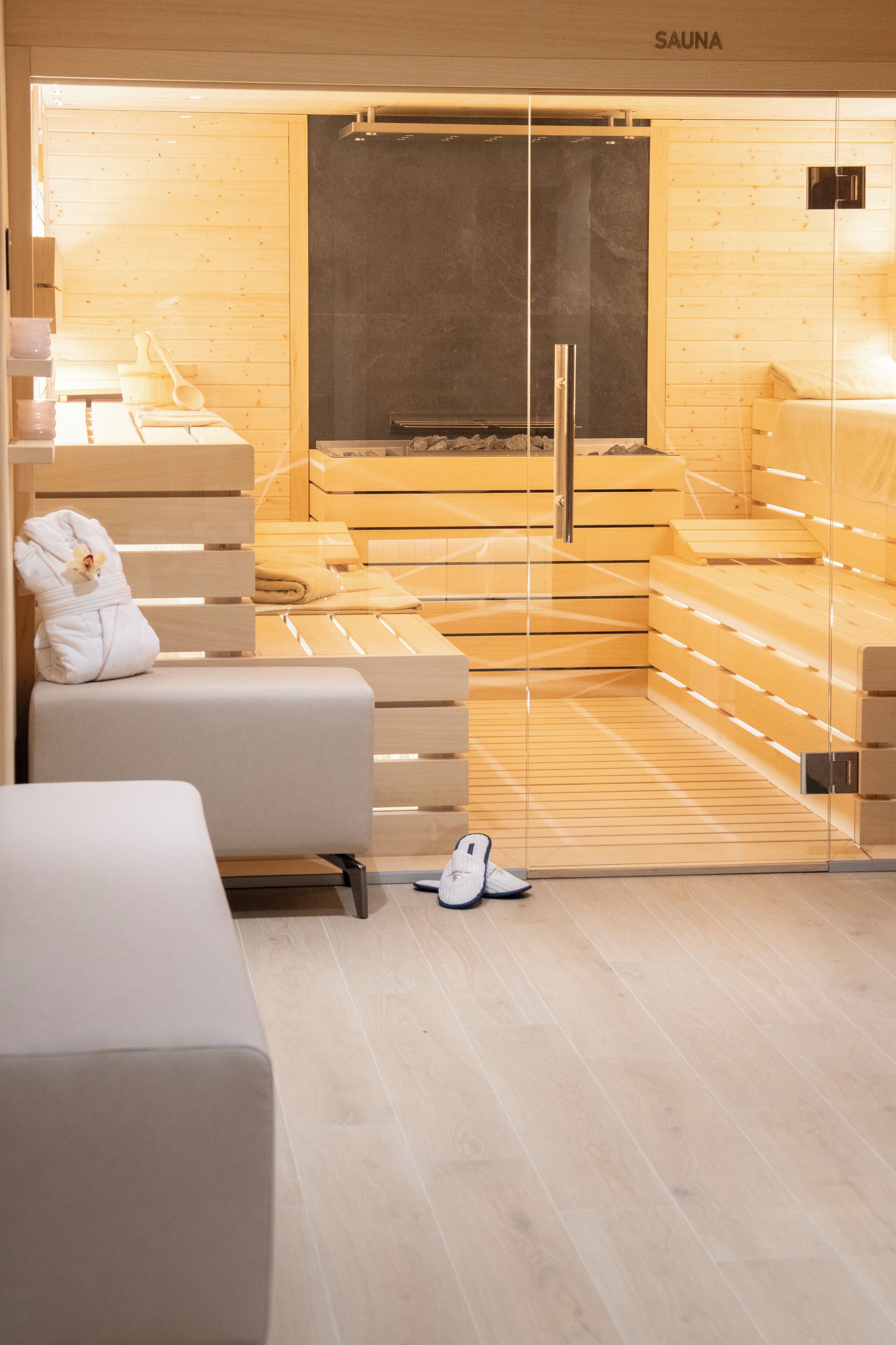 Eine Sauna mit Holzbänken und einer Glastür, ein Handtuch und Hausschuhe auf dem Boden.
