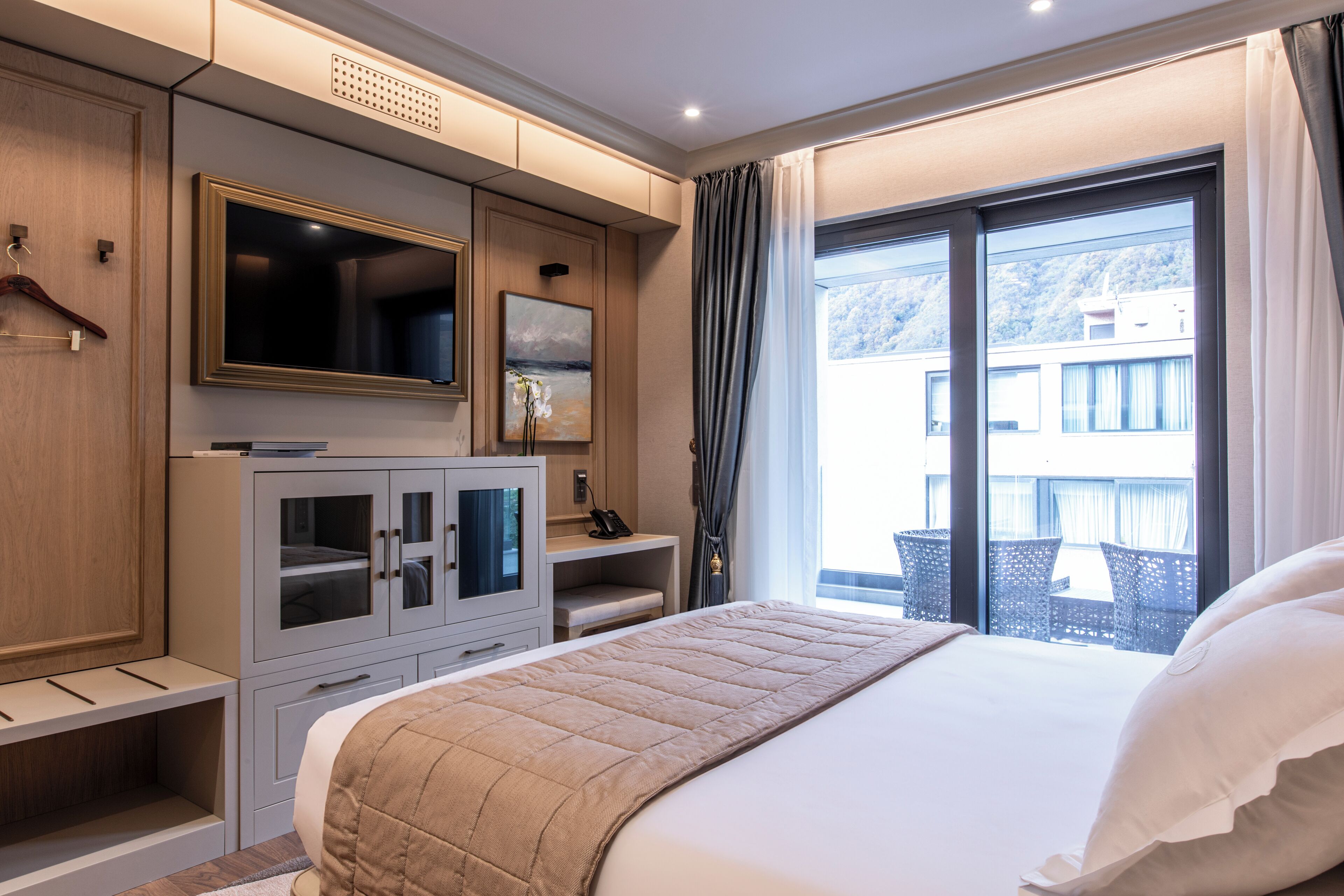 Habitación de hotel con una cama grande, televisión, escritorio y balcón con mobiliario exterior.