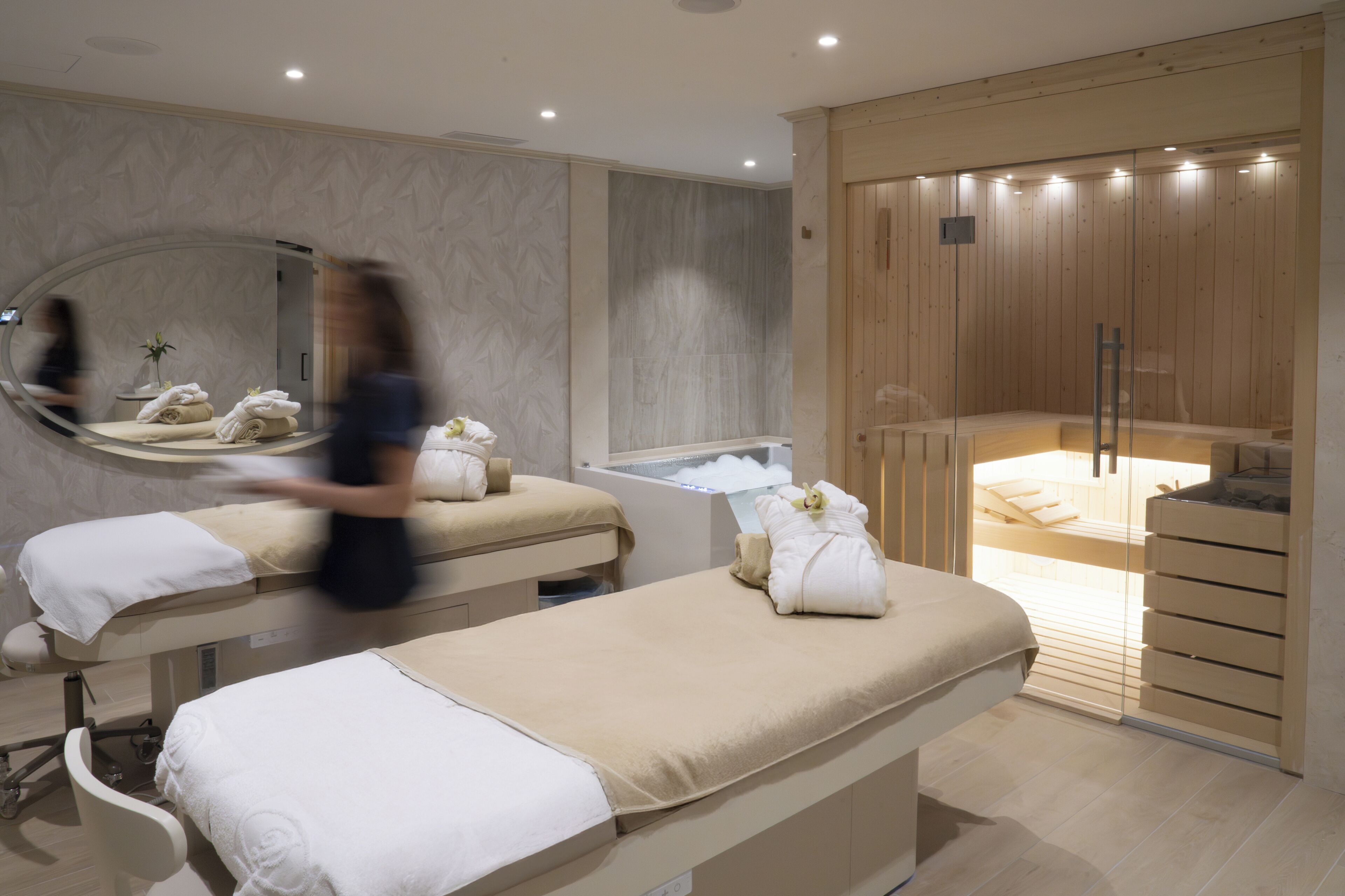 Um espaço de spa com duas mesas de massagem, um espelho grande e uma área de sauna.