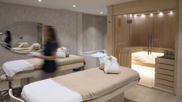 Um espaço de spa com duas mesas de massagem, um espelho grande e uma área de sauna.