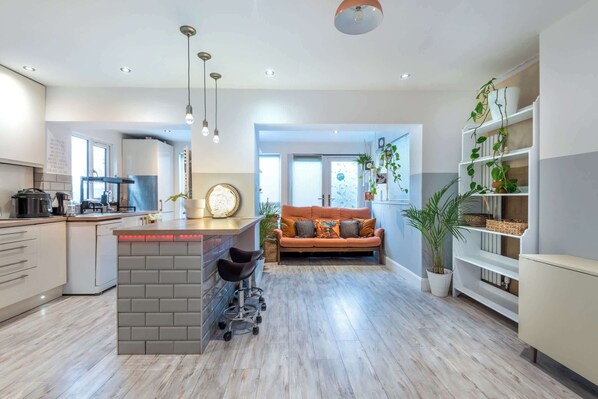A modern kitchen with a central island, a dining area with a sofa, and a living room with a large window.