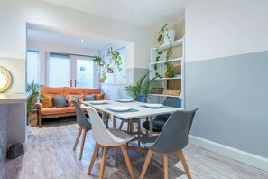 A modern living room with a dining area, a sofa, a coffee table, and a bookshelf with plants.