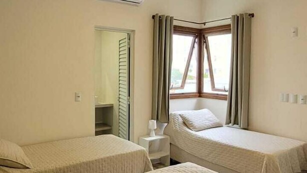A hotel room with two beds, a desk, and a window with curtains. - La Casona (Florianópolis)