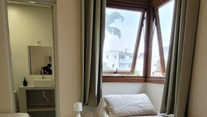 A hotel room with two beds, a small bedside table, a mirror, and a window with curtains. - La Casona (Florianópolis)