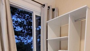 A bedroom with a bed, a window with curtains, a built-in wardrobe, and a small white appliance. - La Casona (Florianópolis)