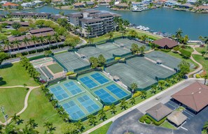 Luchtbeeld van een hotelcomplex met diverse tennisbanen, een jachthaven en omliggend groen.