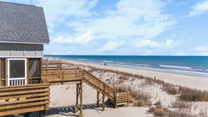 A beach house with a wooden deck and a staircase leading to a sandy beach. - Last Resort - Oceanfront w/ 6-bedrooms (Pawleys Island)