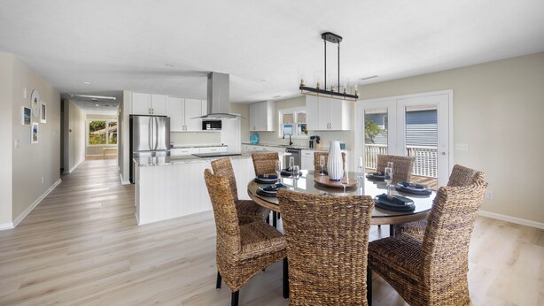 A modern kitchen with white cabinets, a stainless steel refrigerator, and a dining area with wicker chairs and a glass table.