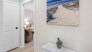 A hallway with a beach-themed painting, a white door, and a small plant on a white dresser.