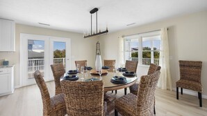 A dining area with a round table, wicker chairs, and a chandelier.