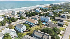 An aerial view of a coastal residential area with houses, a beach, and a pier.