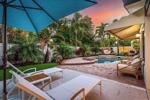 A backyard with a pool, lounge chairs, and a covered patio area.