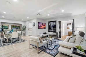 A modern living room with a dining area, a sofa, a coffee table, and artwork on the walls.