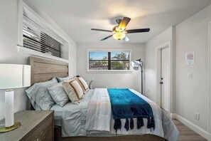 A bedroom with a bed, bedside table, ceiling fan, window, and a door. - Tropical Getaway | Heated Pool & Patio Retreat (Fort Lauderdale)