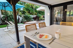 An outdoor dining area with a table set for breakfast, including eggs and bacon, and a coffee cup. - Tropical Getaway | Heated Pool & Patio Retreat (Fort Lauderdale)