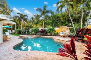 A swimming pool with a curved edge, surrounded by tropical plants and palm trees. - Tropical Getaway | Heated Pool & Patio Retreat (Fort Lauderdale)