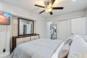 Une chambre à coucher avec un lit, un ventilateur de plafond, un grand miroir et une armoire.