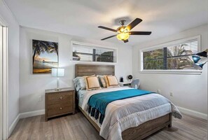 A bedroom with a bed, nightstands, a ceiling fan, a window with blinds, and a wall-mounted lamp. - Tropical Getaway | Heated Pool & Patio Retreat (Fort Lauderdale)