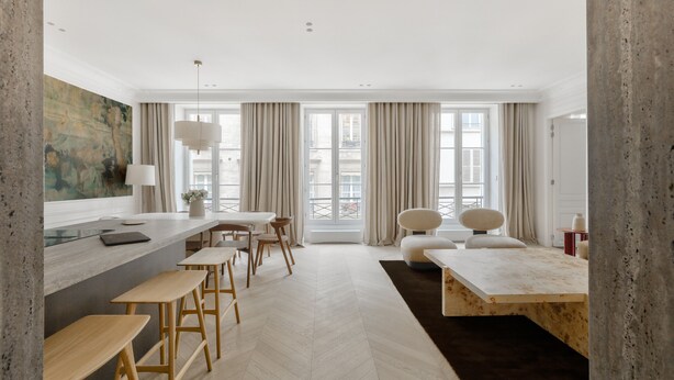 A modern kitchen with a bar area, wooden stools, and a large window with curtains.