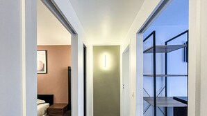 Un pasillo estrecho con una cama, un cuadro enmarcado y una lámpara.