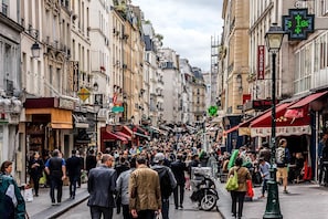 A crowded street with shops and signs, including 'Pizzeria' and 'Boulangerie'.