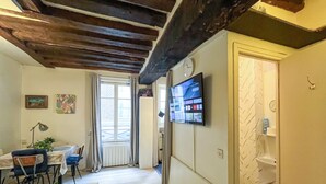 A room with a wooden ceiling, a TV mounted on the wall, a door, and a window with curtains. - Urban Flat 192 - Charming flat - Basfour (París)