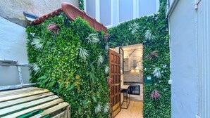 Un espace intérieur étroit, avec un banc en bois, une porte donnant sur une cuisine et des murs recouverts de feuillage verdoyant.
