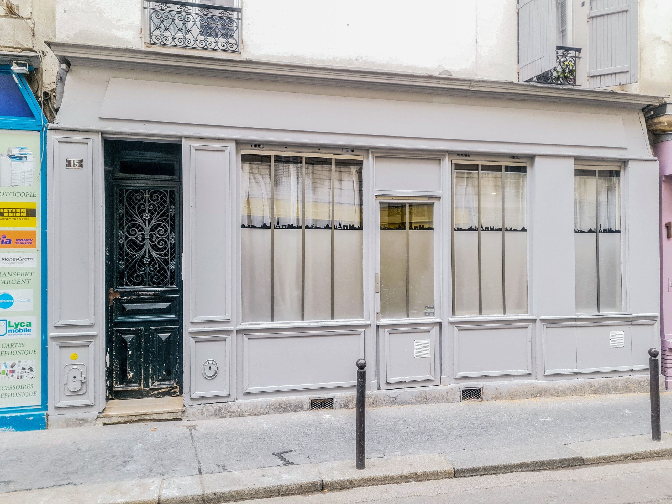 A building with a white facade, a black wrought iron gate, and a blue sign on the left.