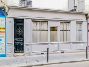 A building with a white facade, a black wrought iron gate, and a blue sign on the left. - Urban Flat 189 - Apartment Montparnasse Vuitton (París)