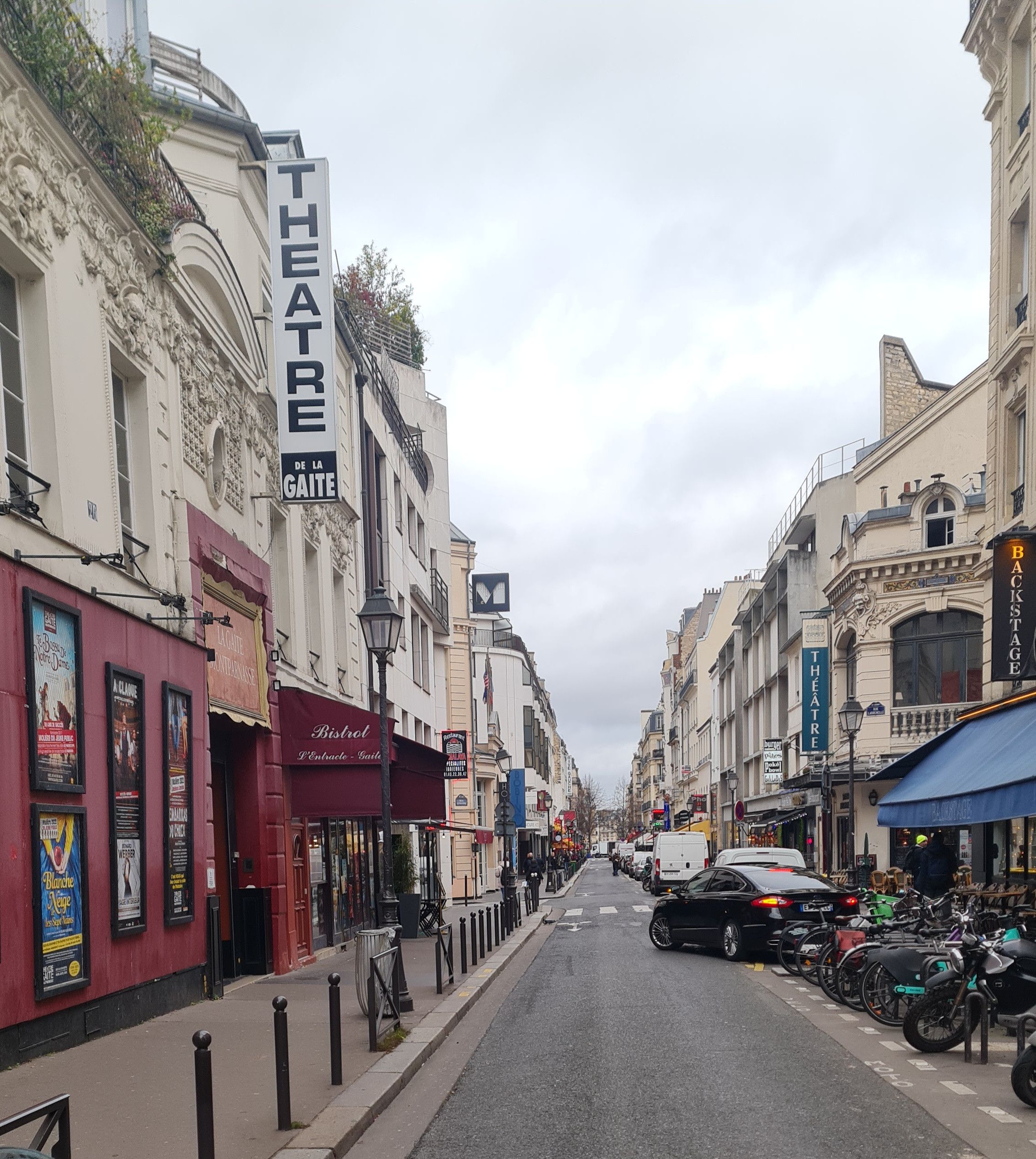 Une rue bordée d’immeubles, dont un théâtre et divers commerces.