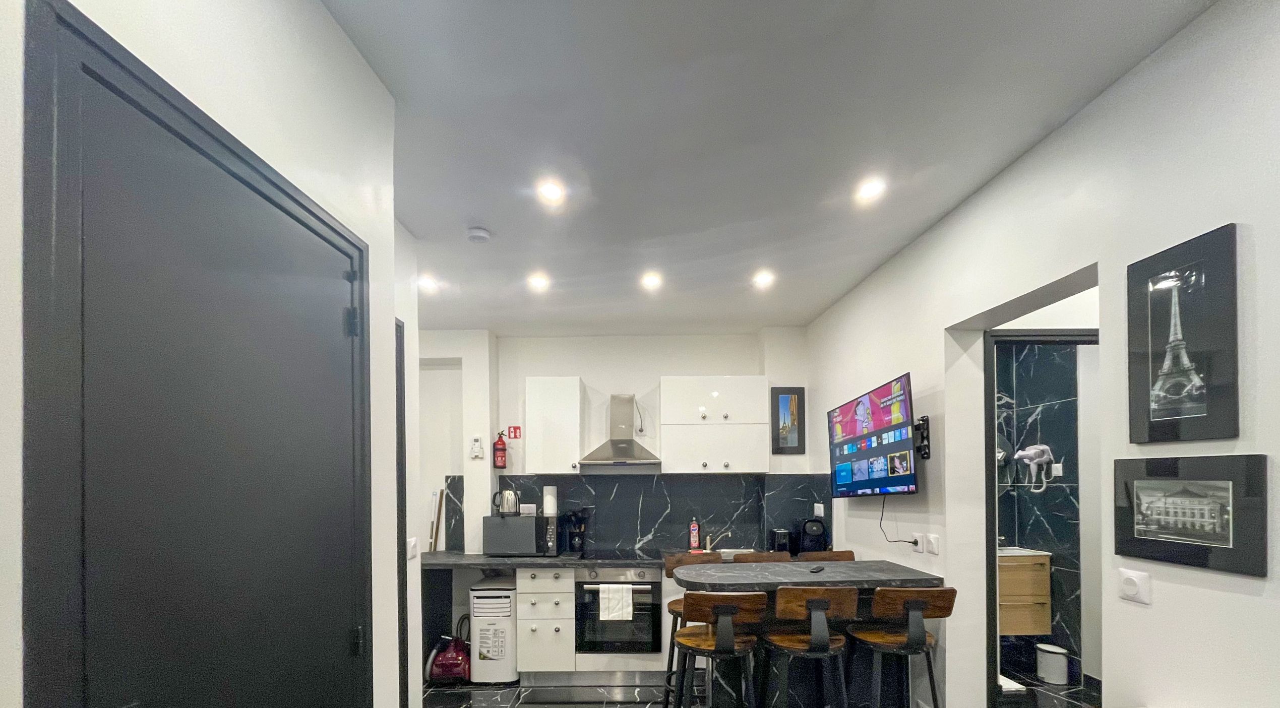 A compact kitchen with a dining area, equipped with modern appliances and a flat-screen TV.