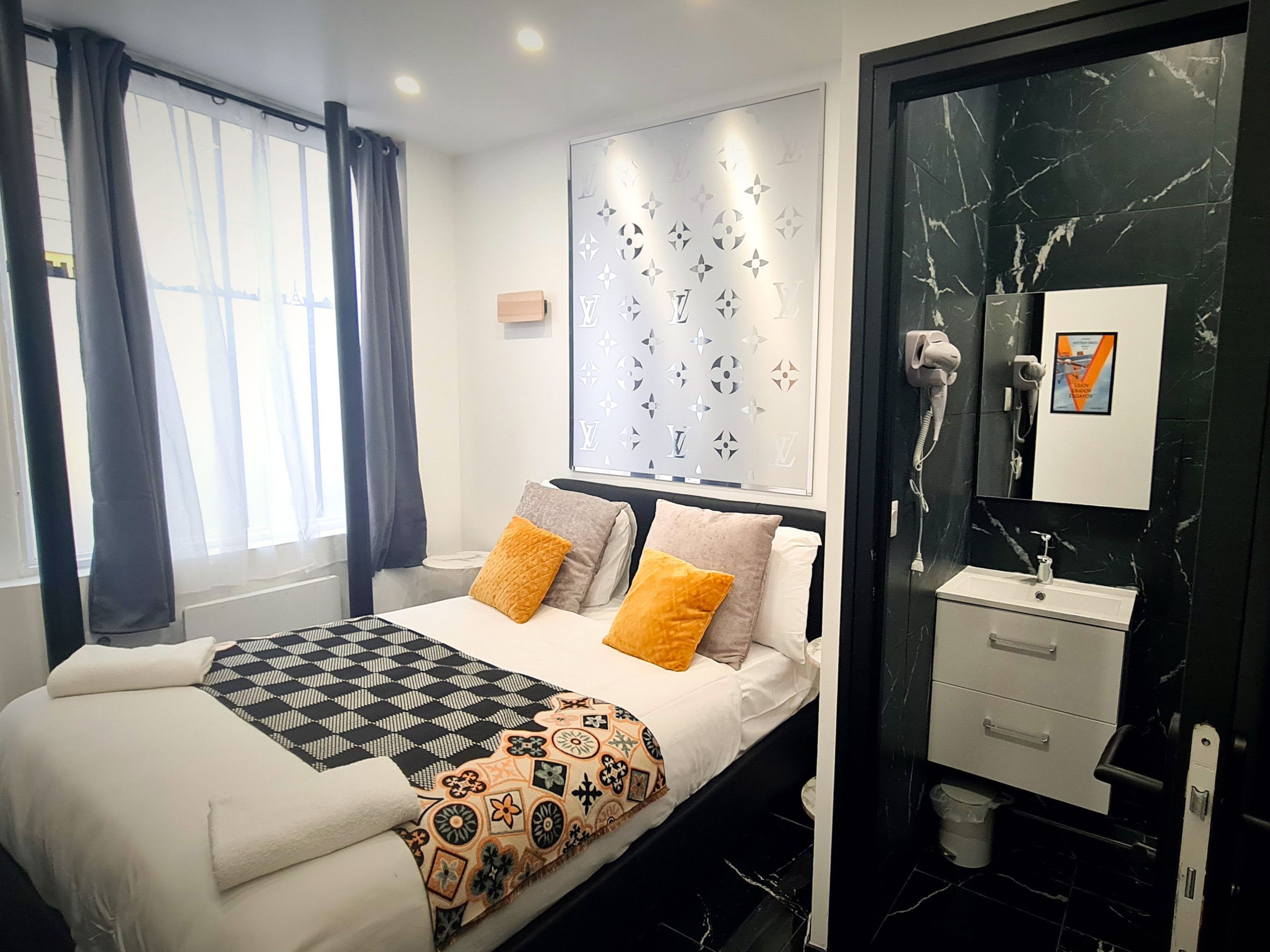 A modern hotel room with a bed, a bathroom with a mirror and sink, and a window with curtains.