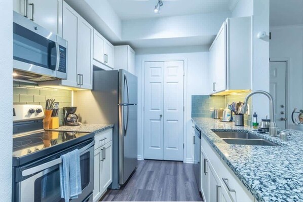 A modern kitchen with white cabinets, a stainless steel refrigerator, a microwave, and a granite countertop.