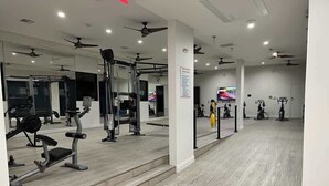 A gym with various exercise equipment, mirrors, and ceiling fans. - Boulevard Stays 1BR King Suite Pool, Gym & Parking 03 (Irving)