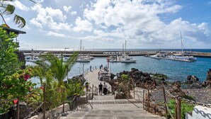 Un port de plaisance avec des bateaux amarrés, un escalier descendant vers l’eau et une côte rocheuse bordée de végétation.