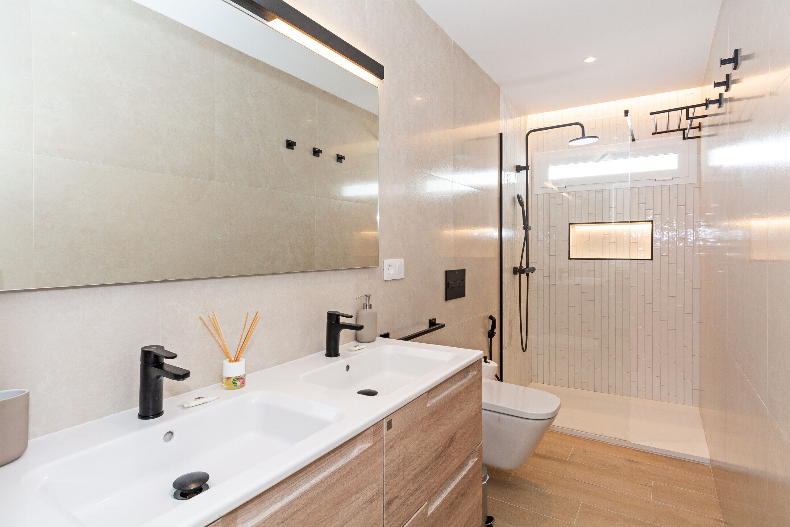 A modern bathroom with a large mirror, dual sinks, and a glass-enclosed shower.