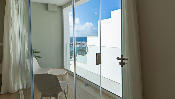 Un balcon avec une porte vitrée, une chaise blanche et une petite table.