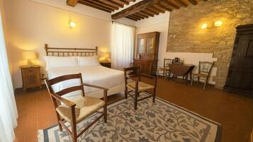A bedroom with a bed, two chairs, a nightstand, a wooden cabinet, and a stone wall.