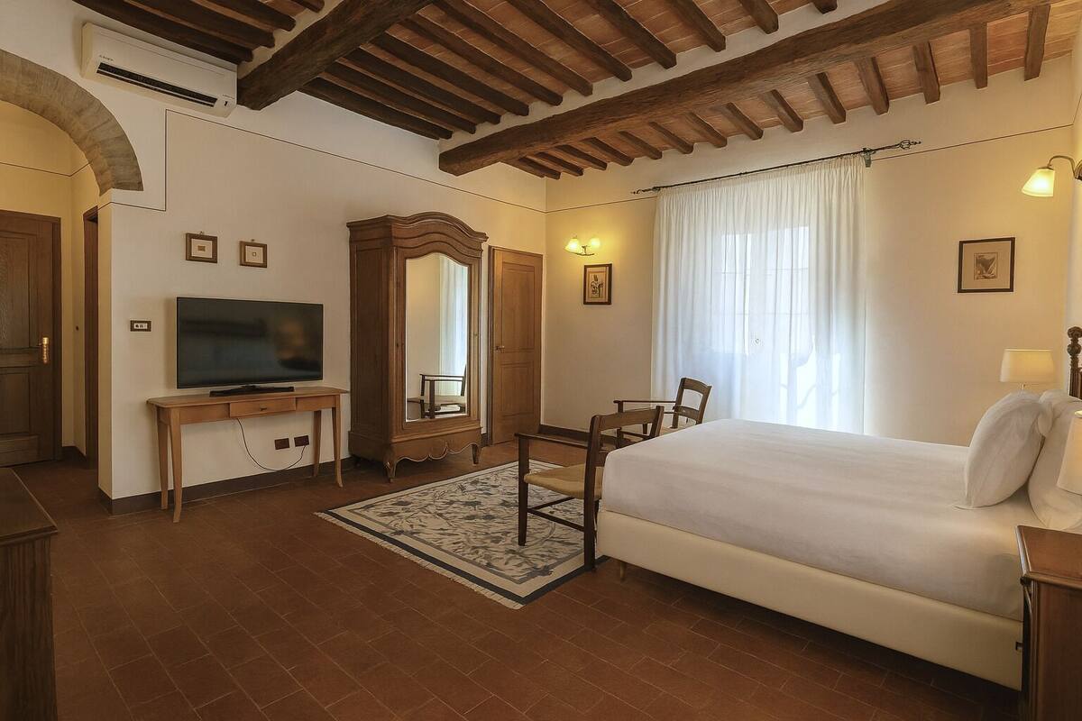 A hotel room with a bed, a TV, a wooden cabinet, a mirror, and a window with curtains.
