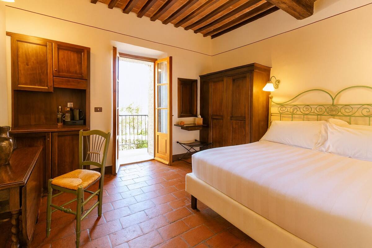 A bedroom with a bed, wooden furniture, a chair, and a balcony door.