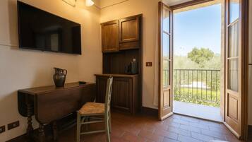 Habitación con escritorio de madera, silla, armarios, televisión y balcón con vista a zonas verdes.