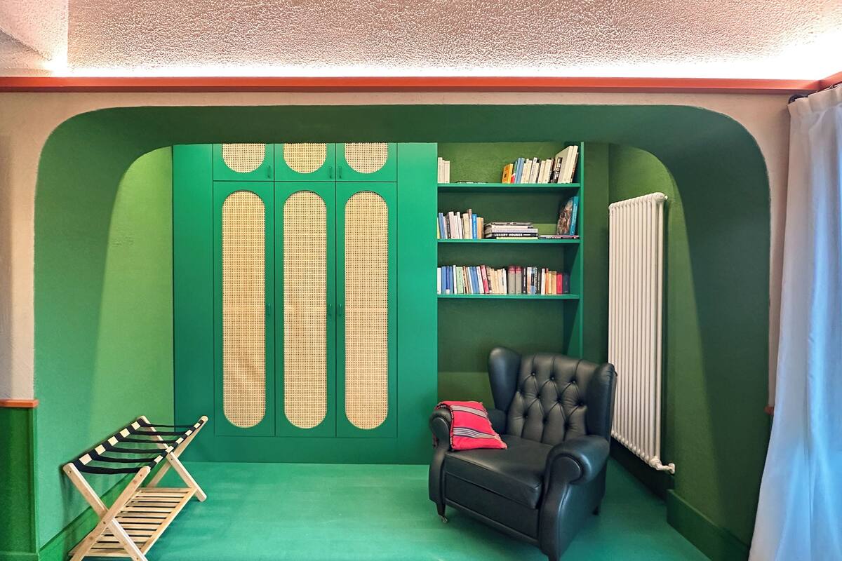 A room with a green wall, a bookshelf, a black leather chair, and a radiator.