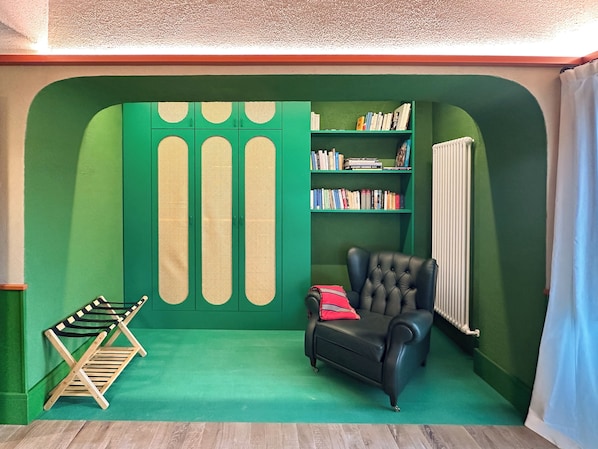 A room with a green wall, a bookshelf, a black leather chair, and a radiator.