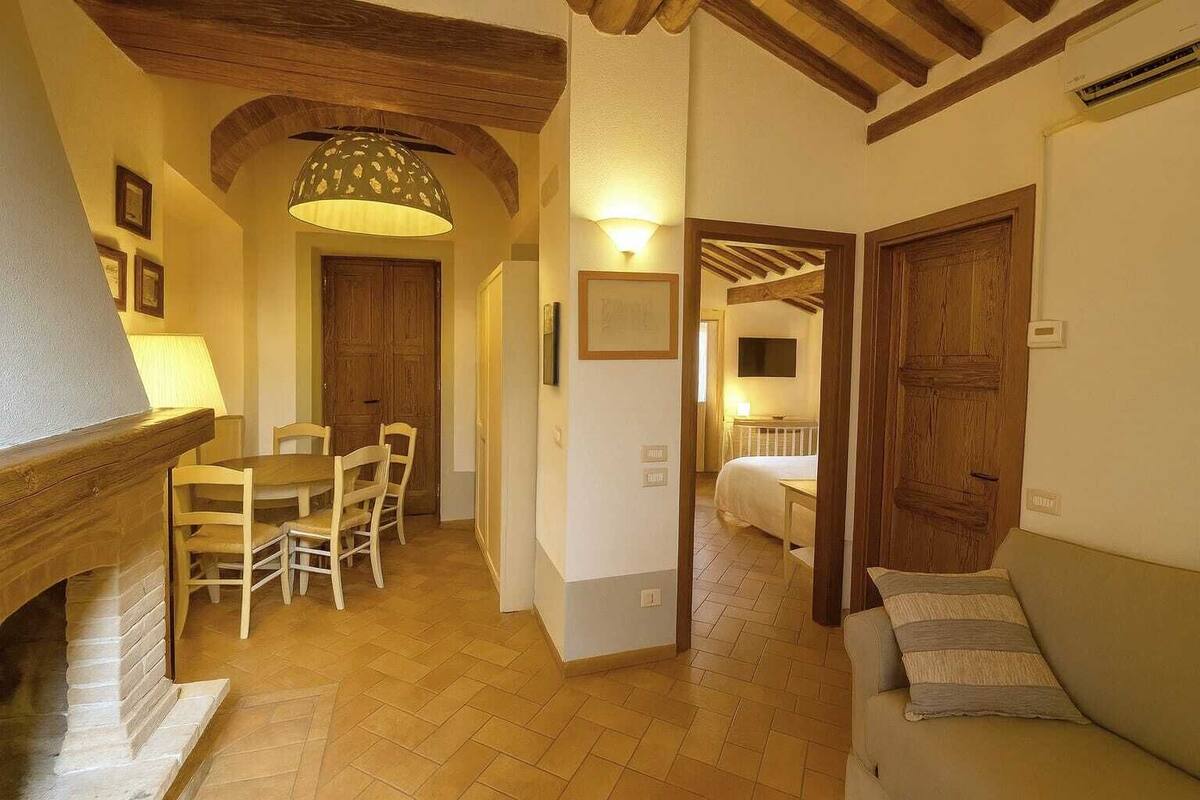 A cozy hallway with a wooden dining table and chairs, a sofa, and a bed in the background.