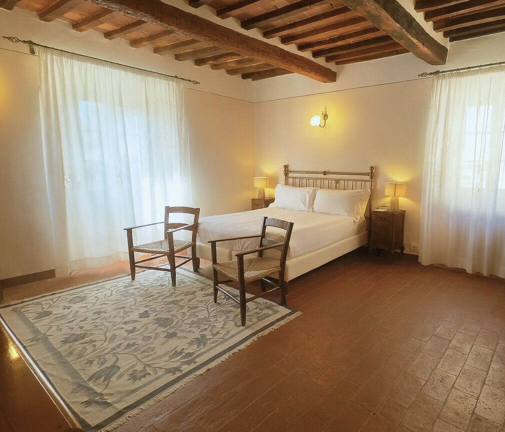Un dormitorio con una cama de madera, dos mesitas de noche con lámparas, una silla y un tapete estampado.
