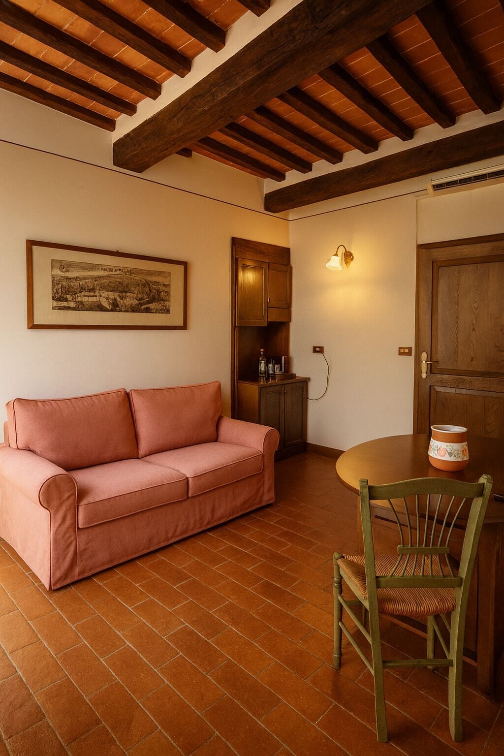 Una habitación acogedora con techo de madera, un sofá rosa, una mesa de comedor de madera con una silla y un armario con una lámpara.