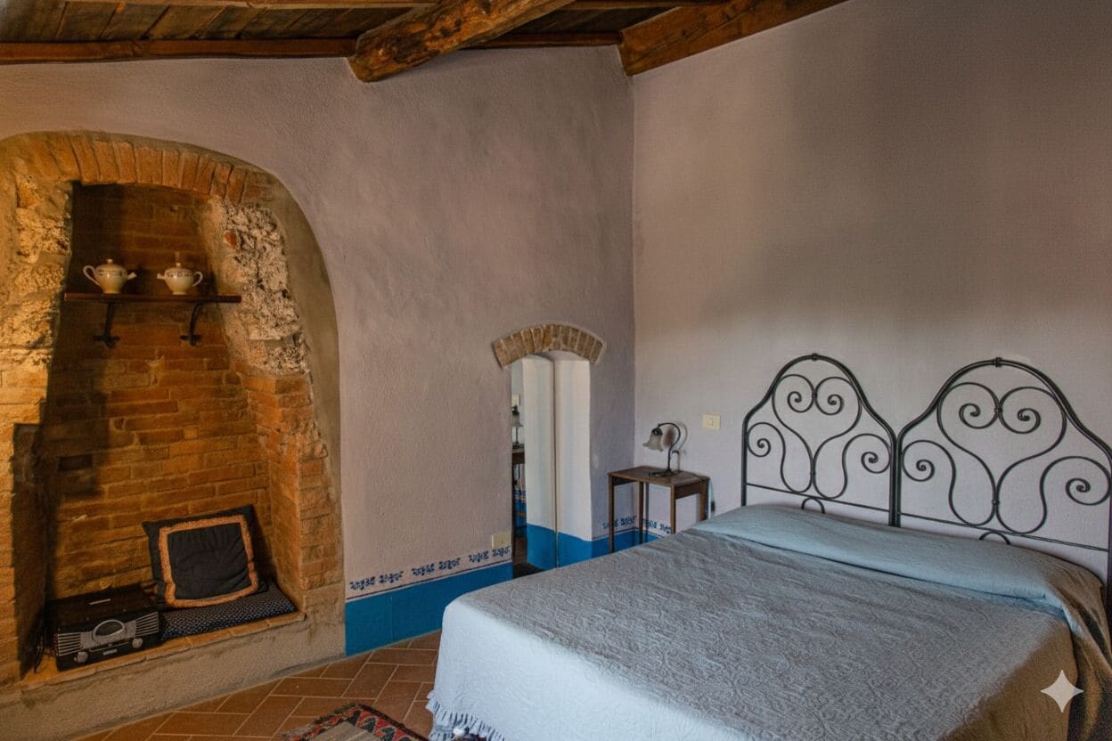 Une chambre avec une cheminée en briques, un lit avec une tête de lit en métal et une petite table avec une lampe.