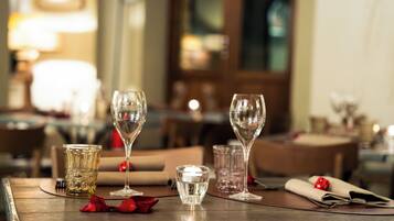 A dining table with clear glassware, a candle, and red rose petals.