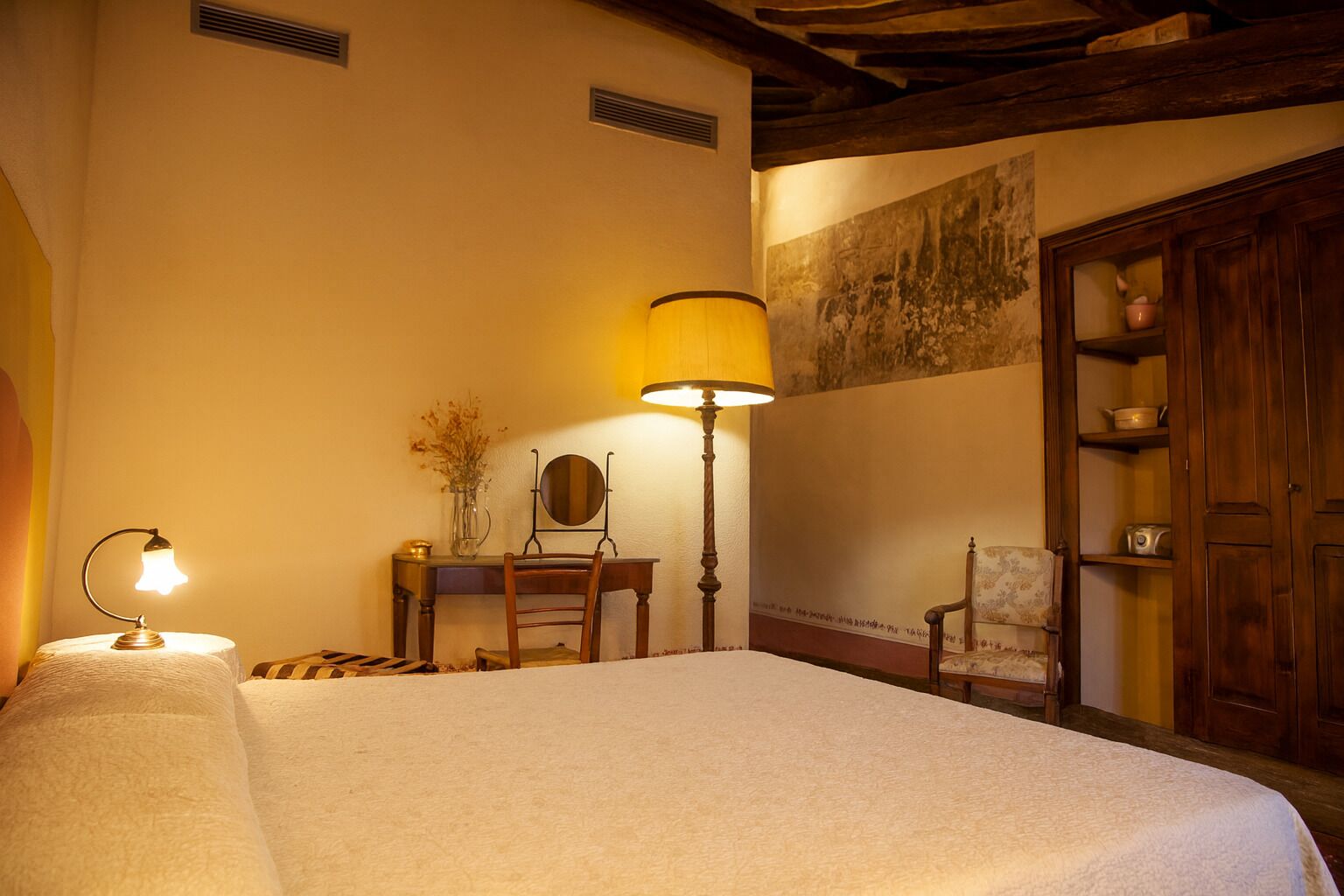 A hotel room with a bed, a desk, a chair, a lamp, and a wardrobe.